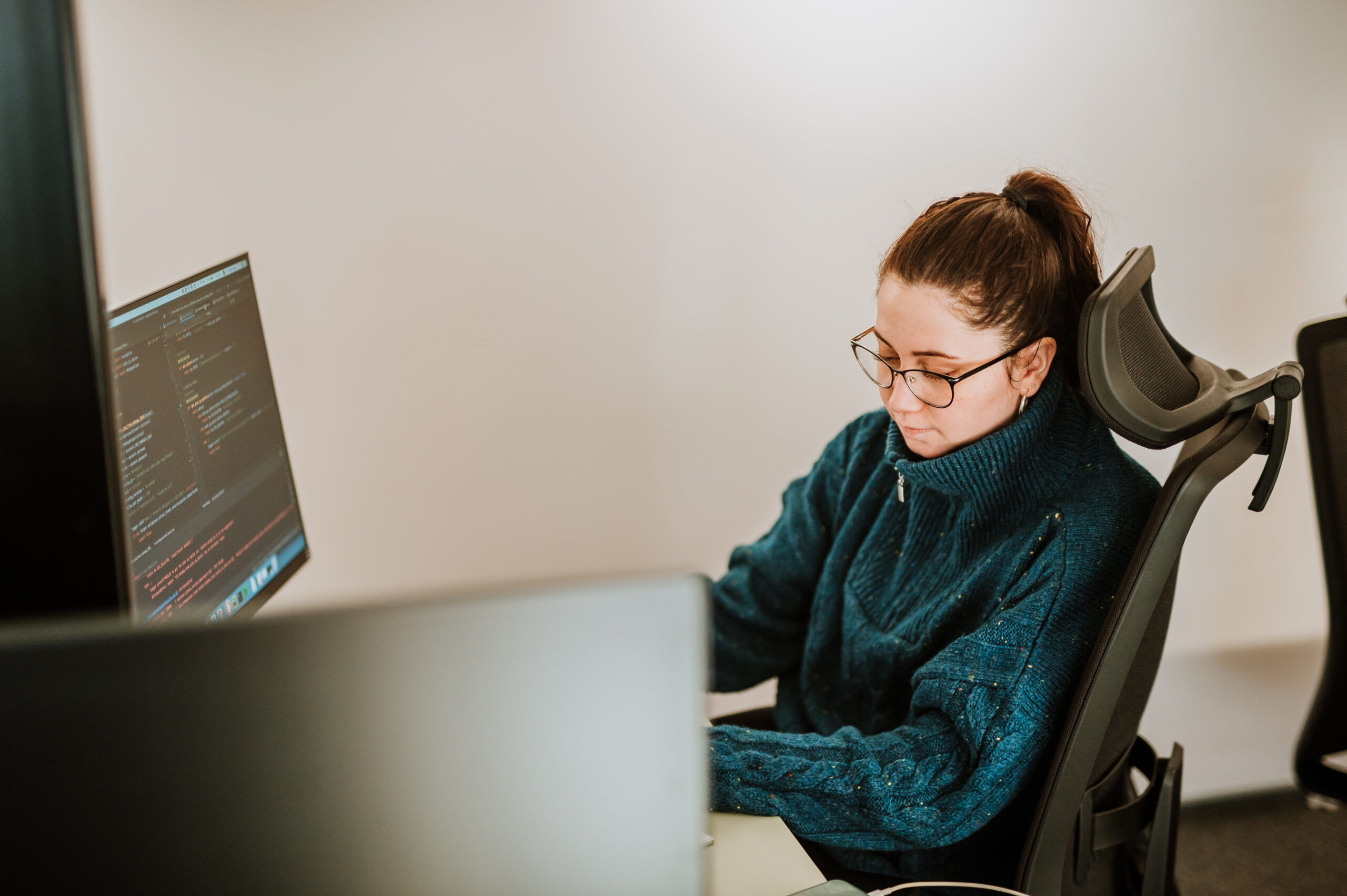 A BetterQA tester in glasses reviewing code on a monitor at her desk