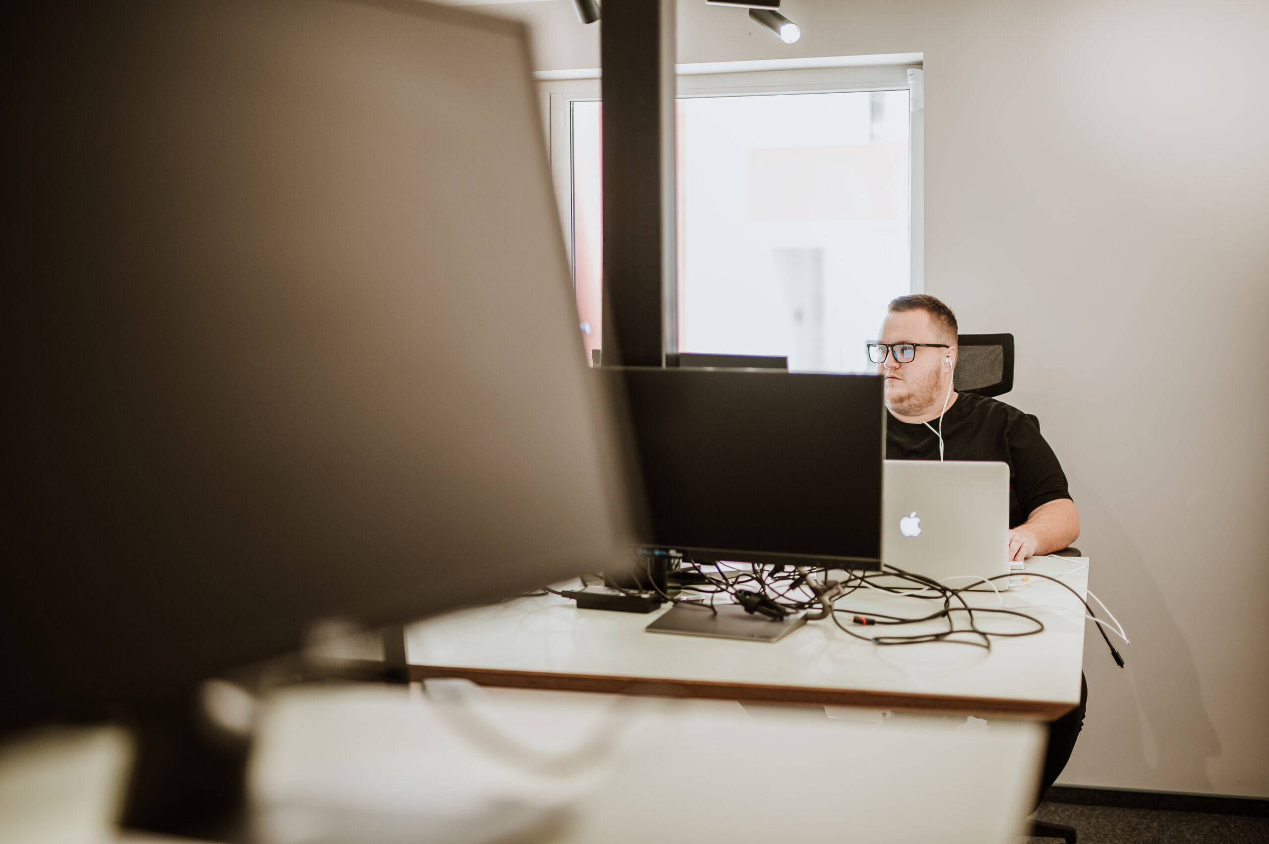 A BetterQA tester at a desk with a laptop, seen past the monitors across the office