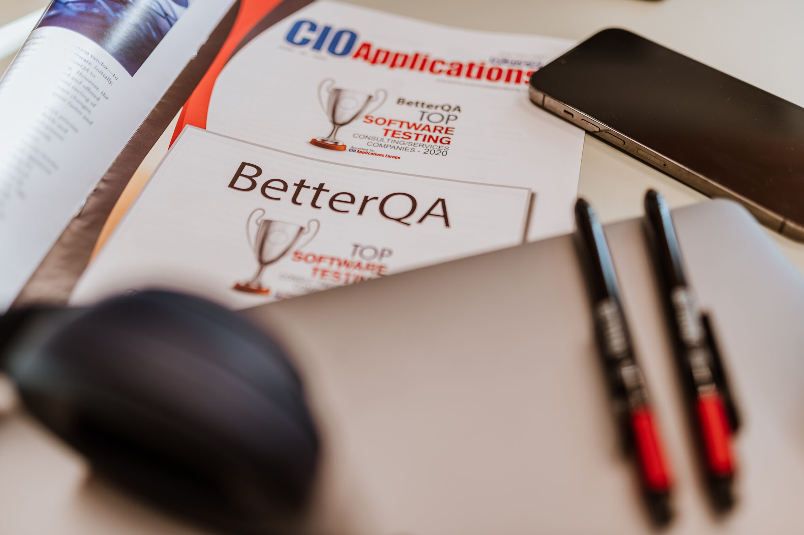 BetterQA desk with a printed software testing award, a phone and pens