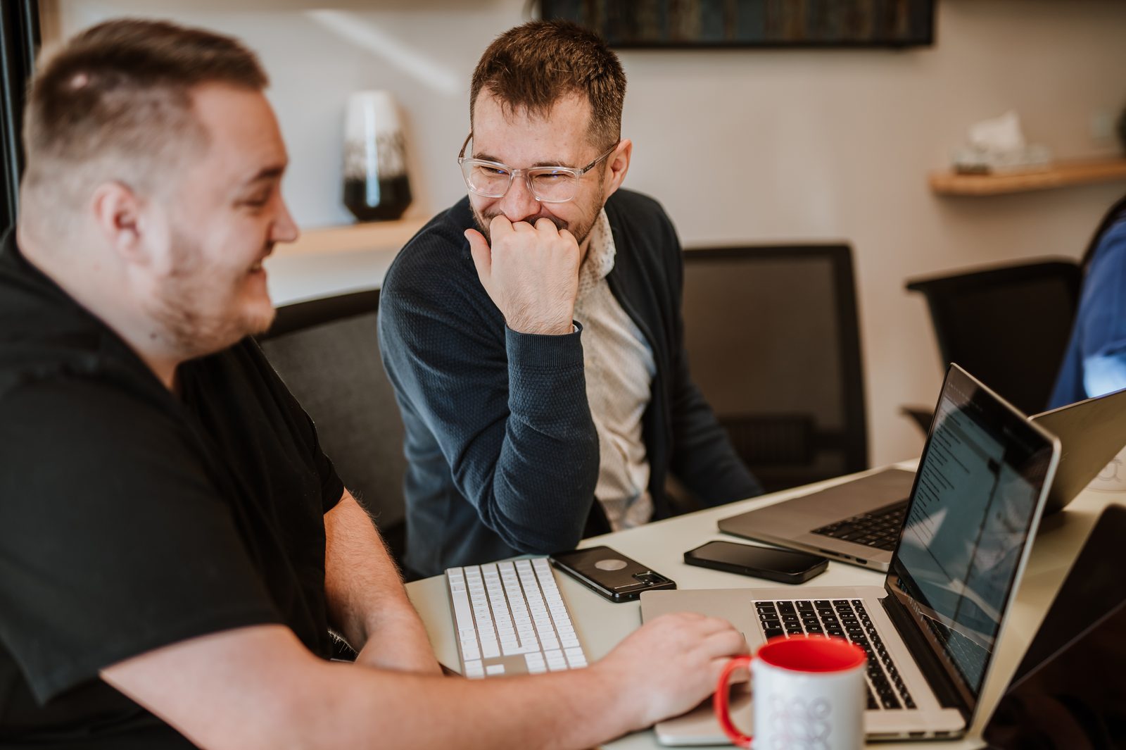 Two BetterQA colleagues laughing together over a laptop in the office